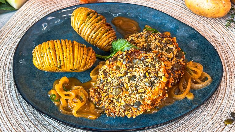 Teller mit gebratenem Kohlrabi im Kürbiskern-Mantel mit Schmorzwiebeln und Fächerkartoffeln.