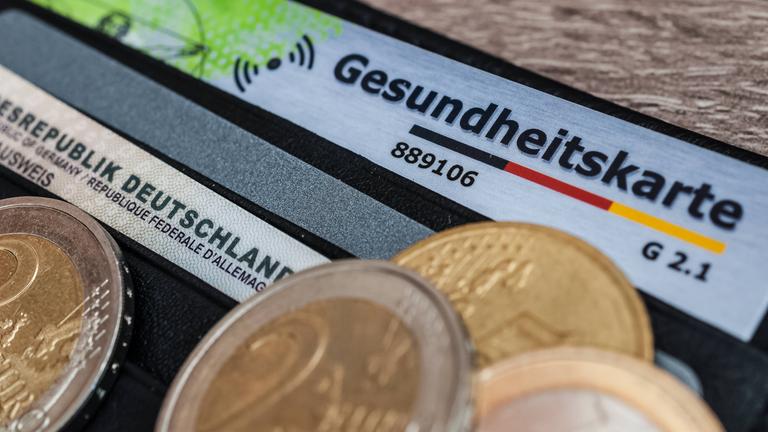 Eine Krankenversicherungskarte mit Kleingeld auf einem Geldbeutel.