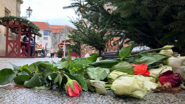 Archiv:  Blumen liegen neben einer Gedenkplatte an den Anschlag auf den Magdeburger Weihnachtsmarkt, während im Hintergrund der Weihnachtsmarkt eröffnet wurde. 