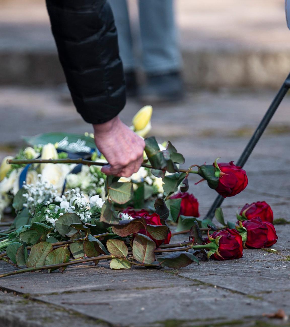 Personen legen Blumen am Trauerkranz im Park Schöntal zum Gedenken an die tödliche Messerattacke in Aschaffenburg ab.