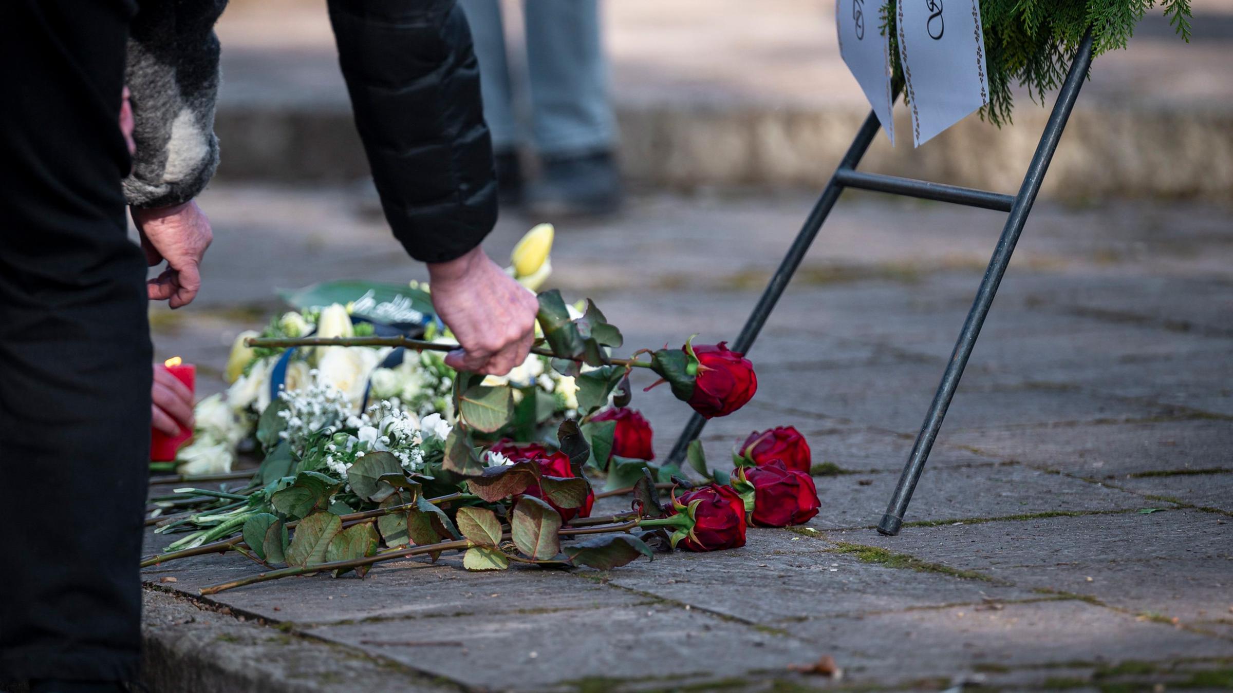 Personen legen Blumen am Trauerkranz im Park Schöntal zum Gedenken an die tödliche Messerattacke in Aschaffenburg ab.