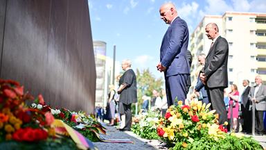 Kai Wegner (CDU, M), Regierender Bürgermeister von Berlin, nimmt während einer Kranzniederlegung an der Mauergedenkstätte Ecke Acker-/Bernauer Straße mit weiteren Teilnehmern an einer Gedenkminute teil. 