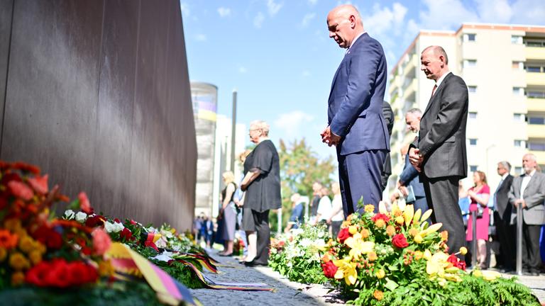 Kai Wegner (CDU, M), Regierender Bürgermeister von Berlin, nimmt während einer Kranzniederlegung an der Mauergedenkstätte Ecke Acker-/Bernauer Straße mit weiteren Teilnehmern an einer Gedenkminute teil. 