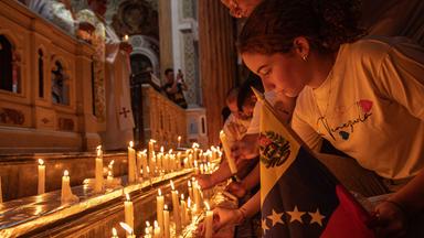 Ein Mädchen zündet eine Kerze während einer Messe an. Vor ihr stehen viele weitere Kerzen zu Gedenken an die Erdbebenopfer in Venezuela.