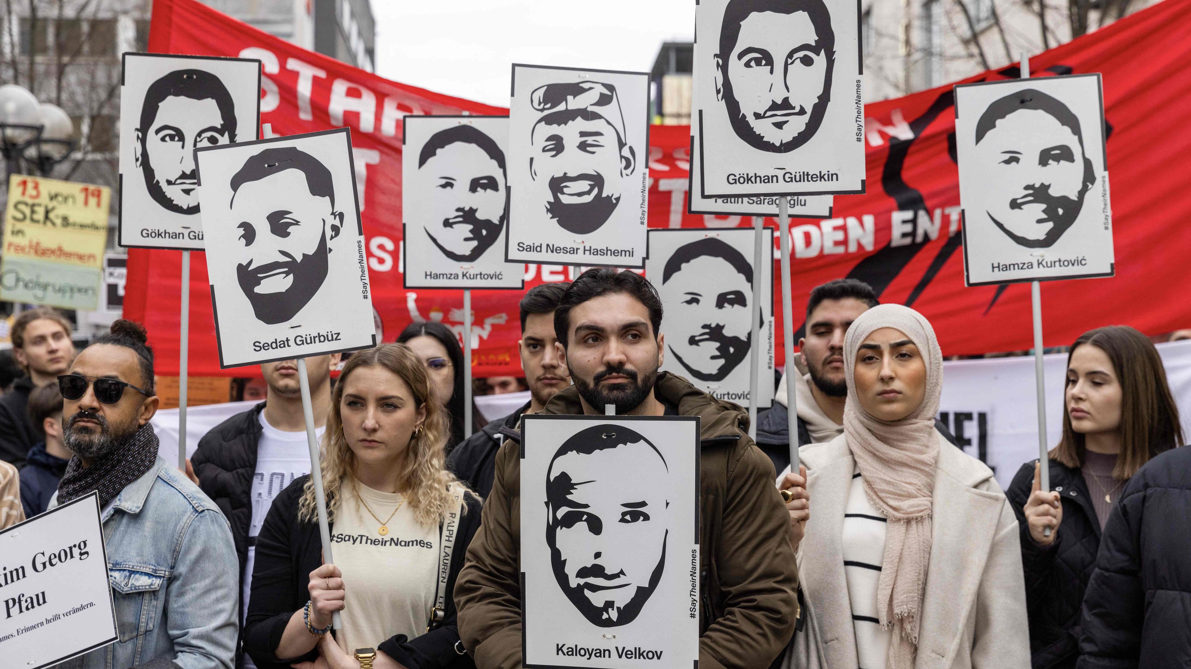 Menschen gedenken an den rassistischen Anschlag von Hanau mit Portraits der Opfer.