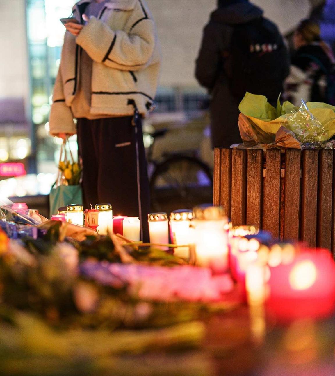 Blumen, Kerzen und handgeschriebene Botschaften bedecken den Boden.
