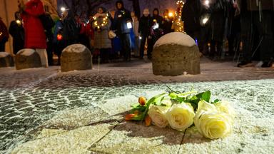  Weiße Rosen und Tulpen liegen auf dem Boden, während Männer und Frauen mit Taschenlampen, Smartphones, Lichterketten und anderen Leuchtmitteln am Geschwister-Scholl-Platz in München leuchten. 