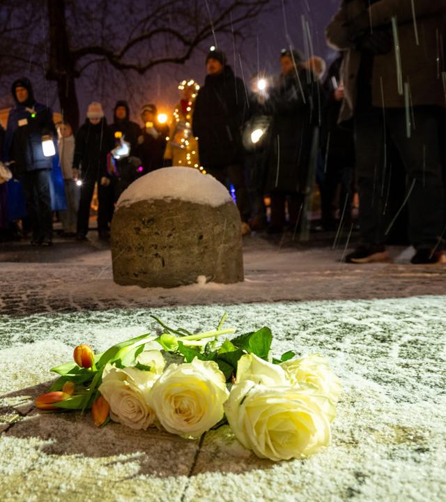  Weiße Rosen und Tulpen liegen auf dem Boden, während Männer und Frauen mit Taschenlampen, Smartphones, Lichterketten und anderen Leuchtmitteln am Geschwister-Scholl-Platz in München leuchten. 