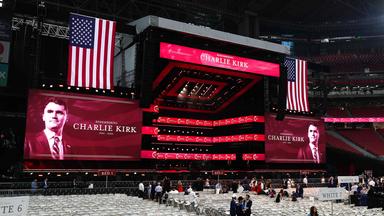 Die Halle für die Gedenkfeier. Eine große Bühne, Bilder von Charlie Kirk und Flaggen der USA