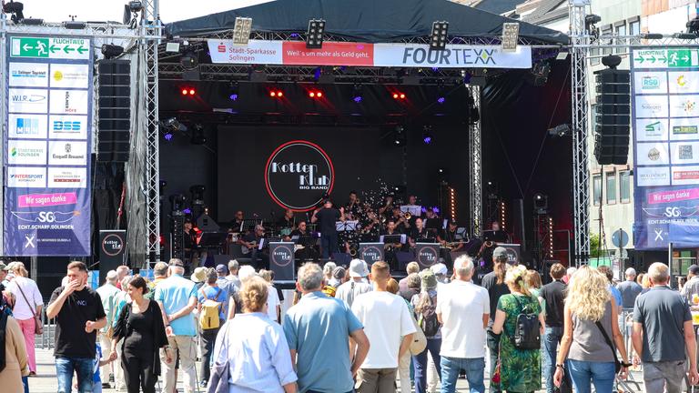 Nordrhein-Westfalen, Solingen: Besucher stehen auf dem Solinger Neumarkt während eines Gedenkkonzerts der Kotten Klub Bigband auftritt.