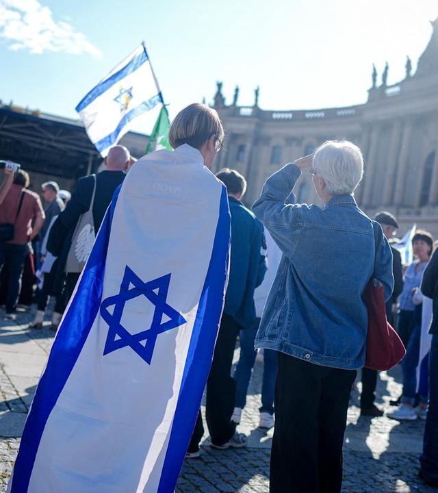 Teilnehmer zeigen die Fahne Israels bei einer Gedenkveranstaltung zum Jahrestag des Terrorangriffs der Hamas auf Israel auf dem Bebelplatz.