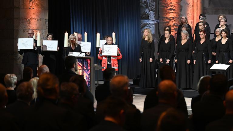 Die Gedenkveranstaltung für die Opfer des Anschlags auf dem Magdeburger Weihnachtsmarkt. Betroffene und Hilfskräfte alten Schilder mit den Namen der Opfer. 