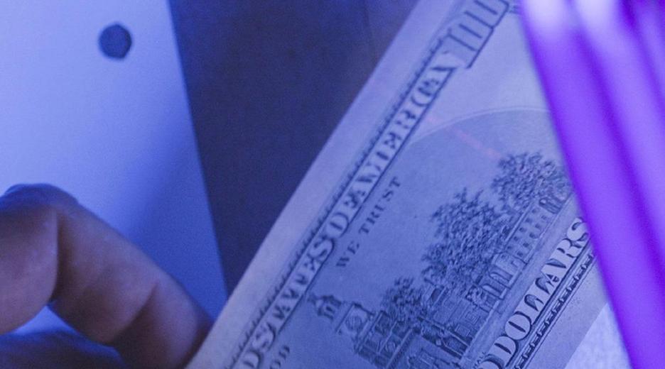 Gefälschte Dollarnote wird unter Schwarzlicht gehalten