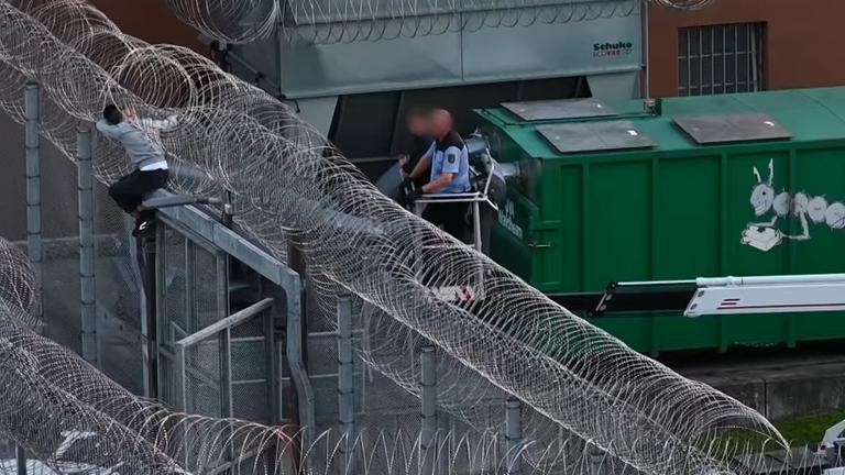 Bei dem Versuch über die letzte Mauer zu klettern, die den 28-Jährigen von seiner Freiheit trennt, bleibt der Insasse im Stacheldrahtzaun hängen.
