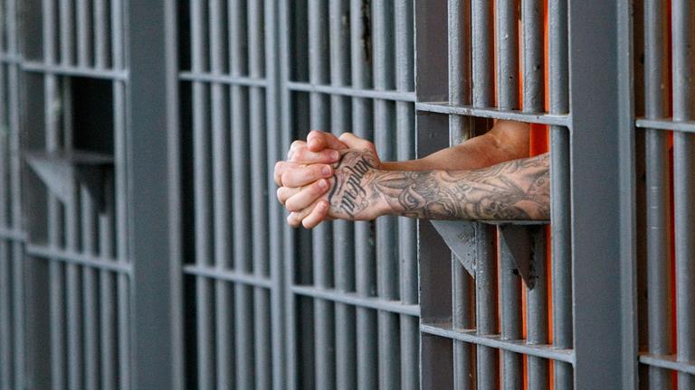 Gefaltete Hände werden durch Gefängnisgitter gestreckt