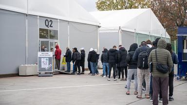 Am ehemaligen Flughafen Tegel stehen Geflüchtete Menschen vor einer Leichtbauhalle.