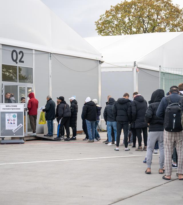 Am ehemaligen Flughafen Tegel stehen Geflüchtete Menschen vor einer Leichtbauhalle.