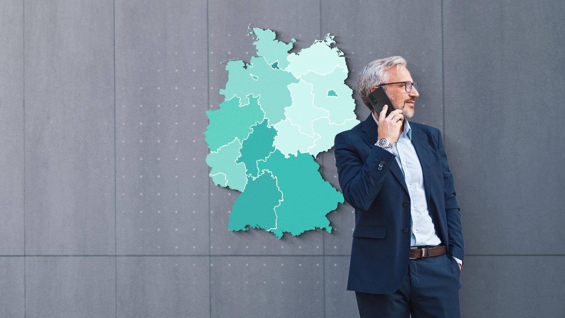 Ein Mann in einem blauen Anzug telefoniert über ein Smartphone. Im Hintergrund ist eine Grafik einer Deutschlandkarte mit in unterschiedlichen Grüntönen markierten Bundesländern zu sehen.