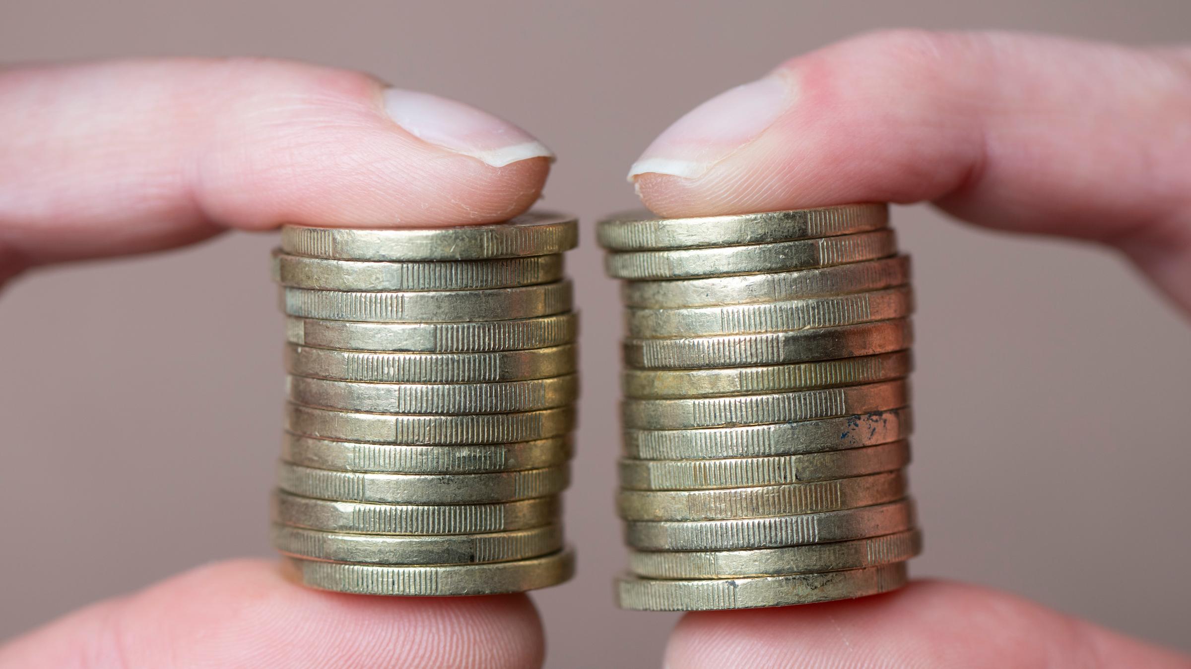 Eine Frau hält gestapelte Euro-Münzen zwischen Daumen und Zeigefinger.