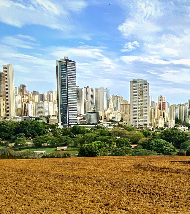 Montage: Vorne ein frisch gepflügtes Feld; im Hintergrund die Skyline einer nahen Großstadt