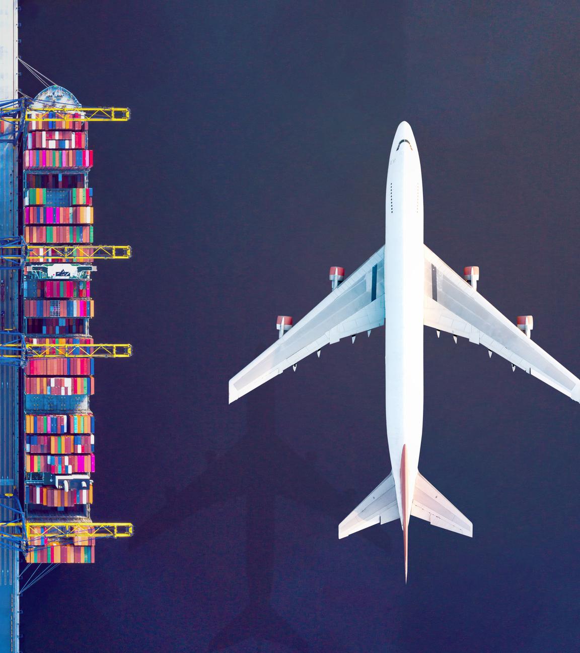 Ansicht von oben; ein Frachthafen, rechts und links Containerschiffe, in der Mitte ein weißes Fracht-Flugzeug.