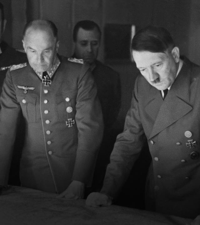 Schwarz-Weiß-Aufnahme von 1941: Militärs der Wehrmacht sowie NS-Diktator Adolf Hitler stehen dicht um einen großen Kartentisch und beraten militärische Operationen.