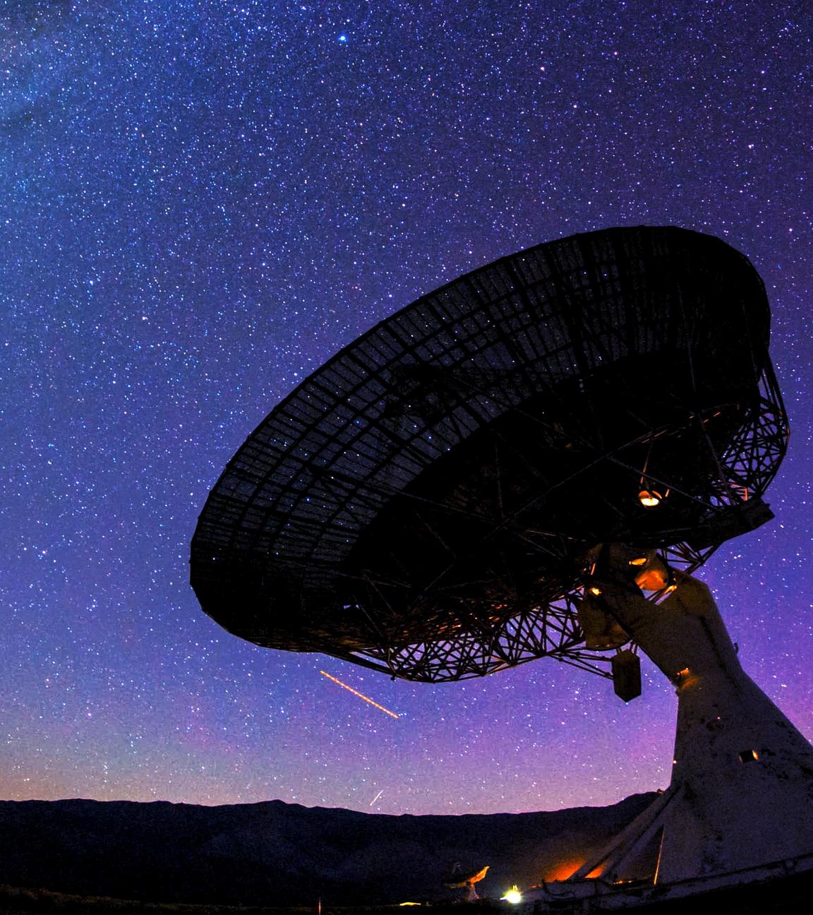 Ein riesiges Teleskop steht vor dem Nachthimmel. Dahinter ist die Milchstraße zu sehen.