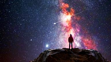 Ein Mann steht auf einem Berggipfel und beobachtet das Universum