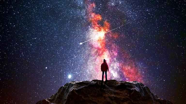 Ein Mann steht auf einem Berggipfel und beobachtet das Universum