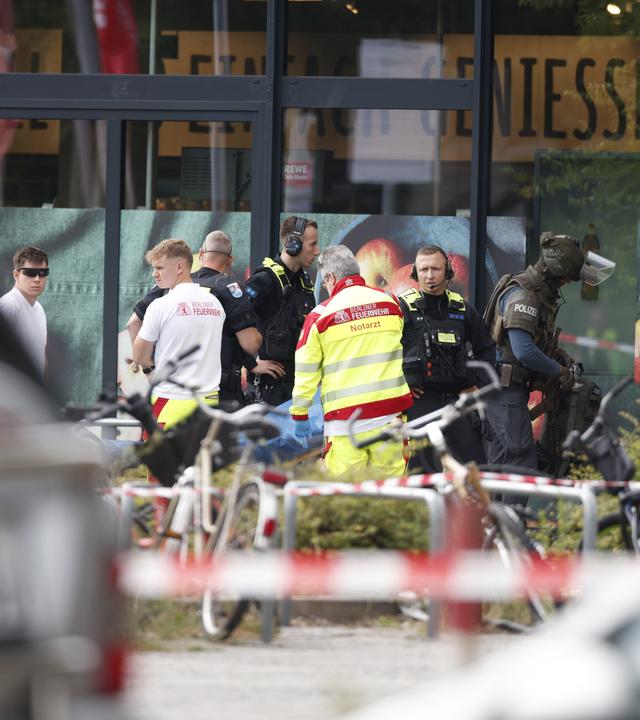 11.07.2026, Berlin: Einsatzkräfte stehen vor einem Supermarkt neben einer verletzten Person auf einer Trage.