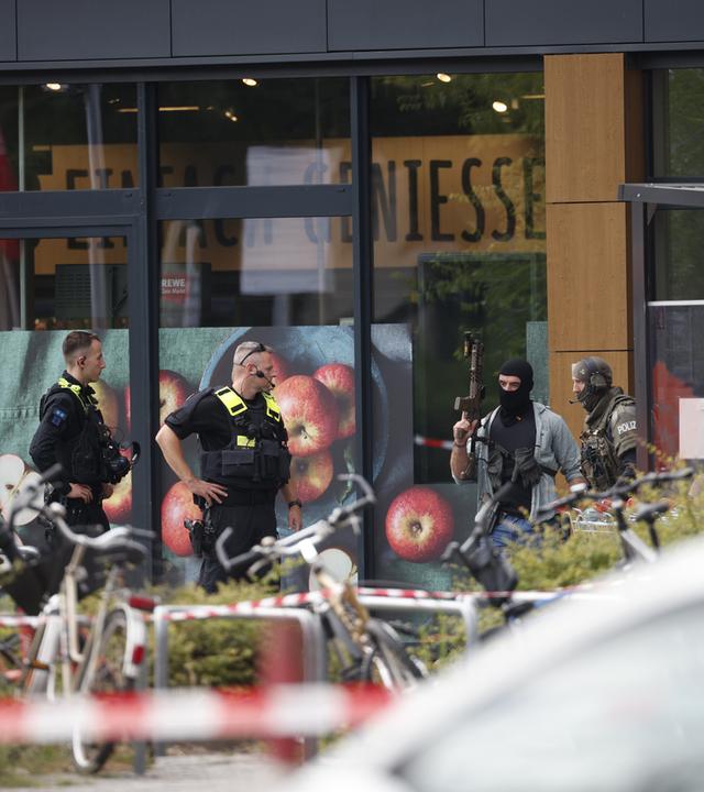 Einsatzkräfte stehen am 11.07.2026 vor einem Berliner Supermarkt, in dem ein Mann seit dem Vorabend eine Frau als Geisel hält.