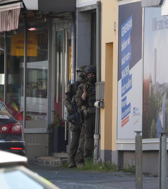 Einsatzkräfte der Polizei stehen an einem Einsatzort einer Geiselnahme in einer Bankfiliale im rheinland-pfälzischen Sinzig. Die Einsatzkräfte sind mit einem Großaufgebot im Kreis Ahrweiler vor Ort.