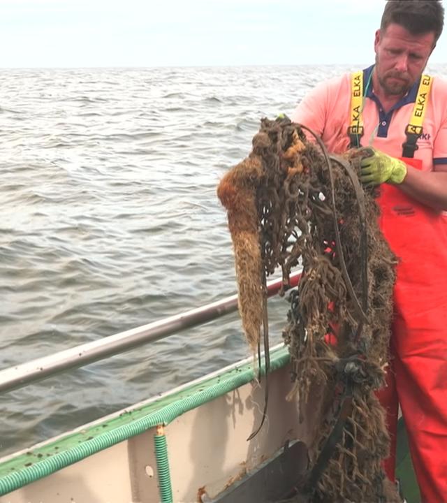 Ein Mann schaut sich ein altes Fischernetz an.