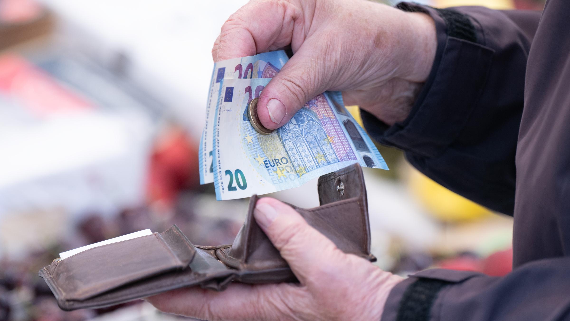 Blick auf Hände, die ein Portemonnaie und mehrere Geldscheine sowie eine Euro-Münze halten
