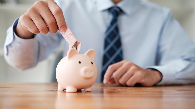 Mann steckt Geldschein in Sparschwein