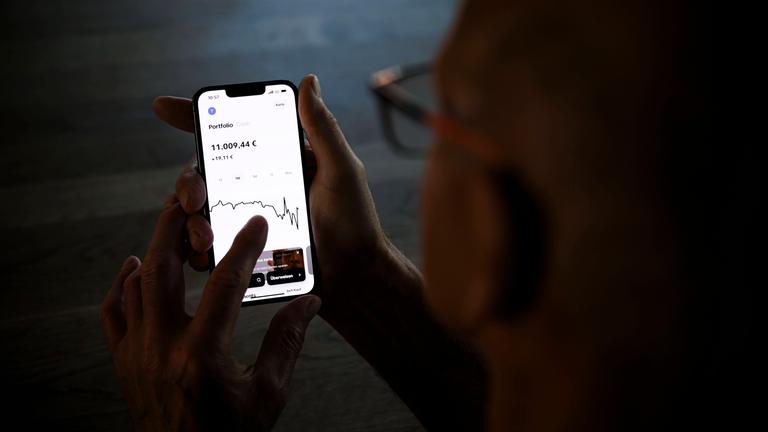 Ein älterer Mann hält ein Smartphone mit einer Trading-App in den Händen am 05.09.2024 in Berlin.