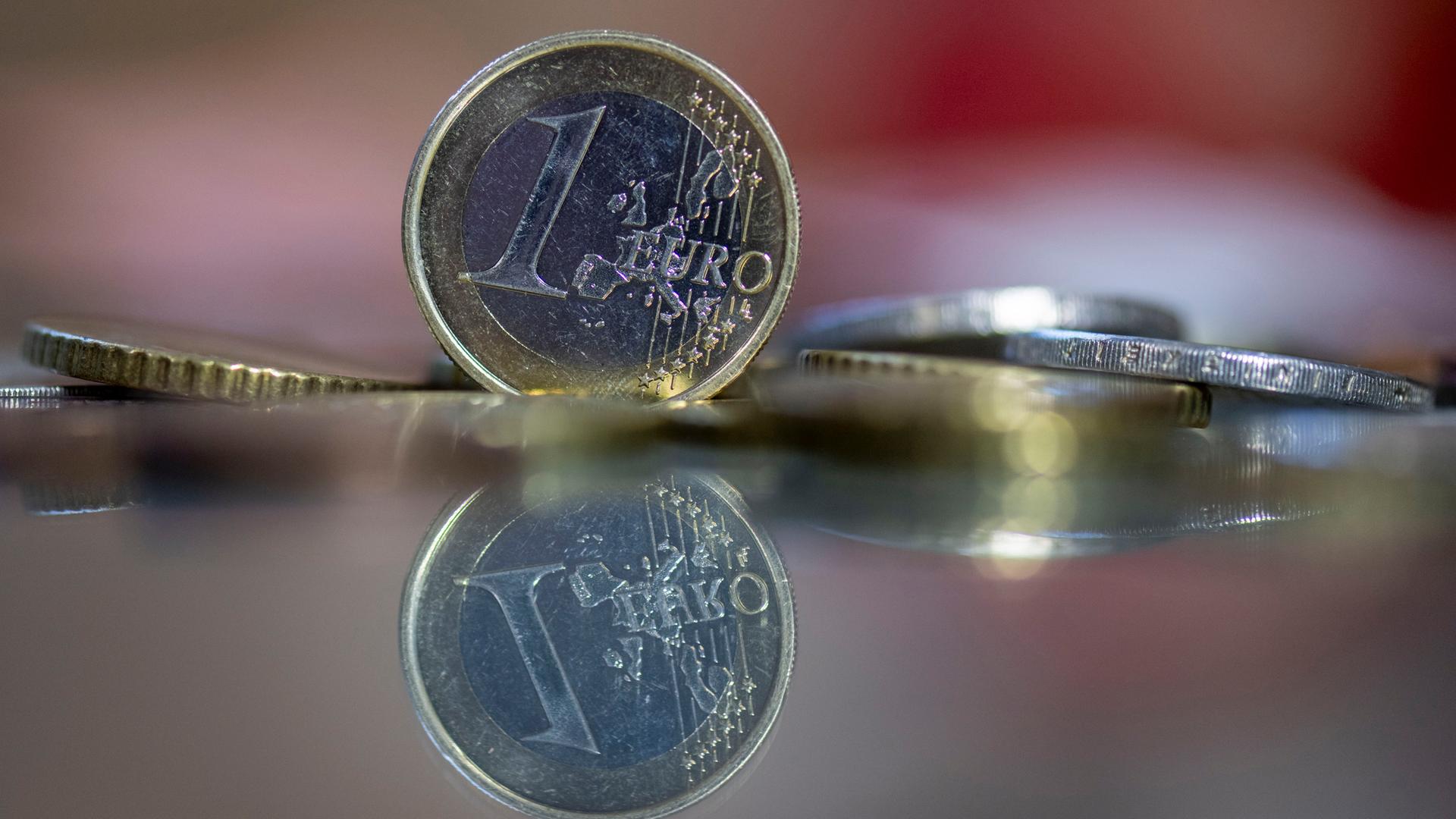 Eine 1-Euro-Münze steht auf einem Tisch, umgeben von anderen Euro-Münzen