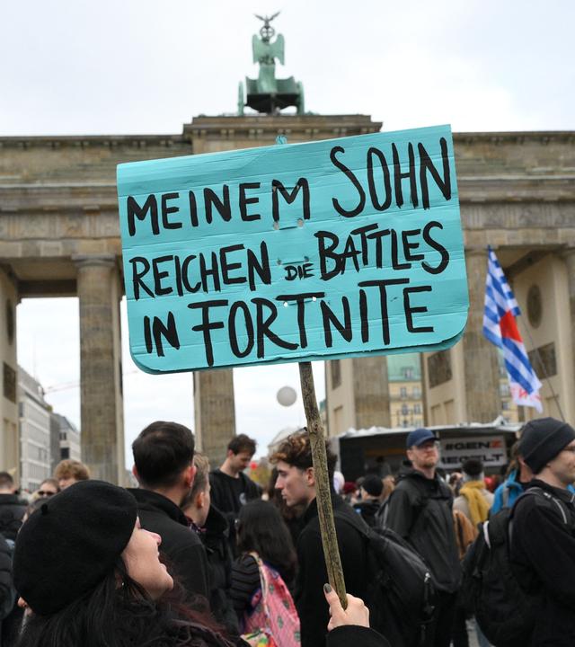 Eine Demonstrantin hält während einer von „GenZ regelt!“ organisierten Demonstration am 31.10.2026 in Berlin ein Schild mit der Aufschrift „Die Kämpfe in Fortnite reichen meinem Sohn schon“ hoch. 
