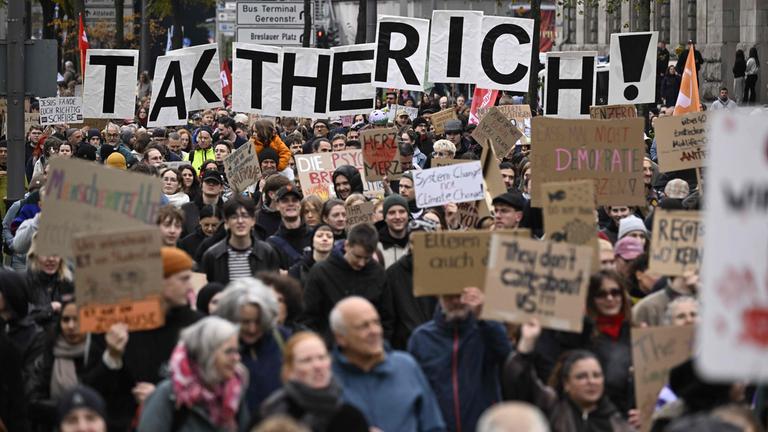 Demonstranten halten bei einer von „GenZ regelt!“ organisierten Kundgebung am 31.10.2026 in Köln Schilder mit der Aufschrift „Tax The Rich“ hoch.