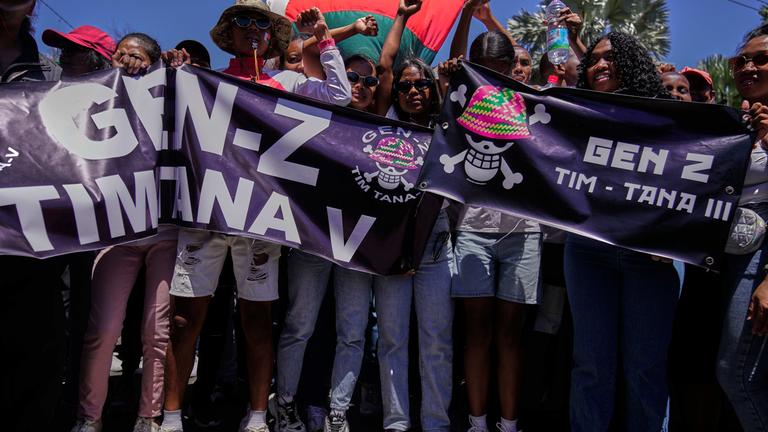 Mehrere Jugendliche und junge Erwachsene halten auf einer Demonstration in Madagaskar Banner und Fahnen.