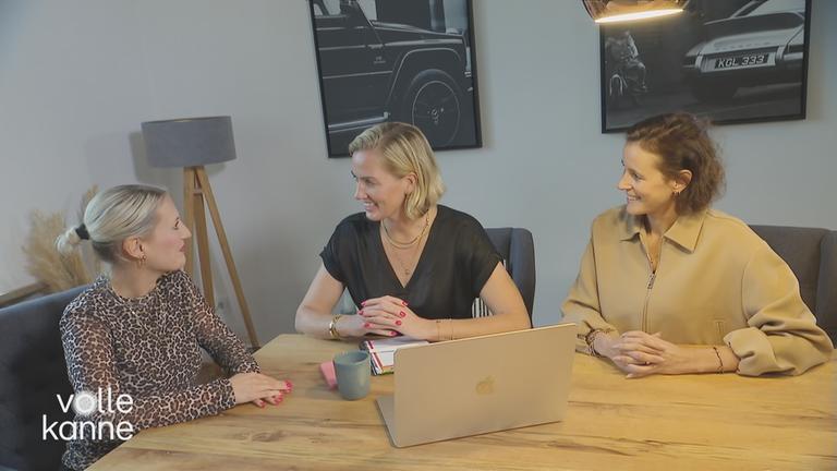 Drei Frauen an einem Tisch unterhalten sich. Auf dem Tisch steht ein Laptop.