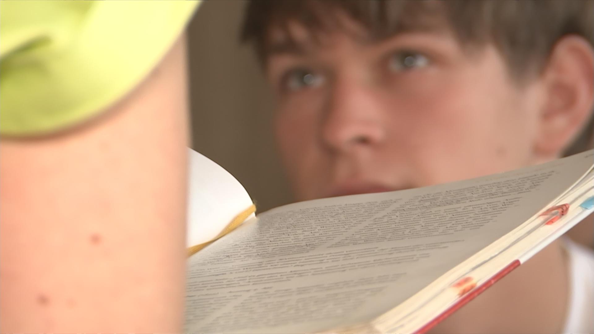 Auf dem Bild ist ein offenes Buch zu sehen und im Hintergrund ein Schüler.