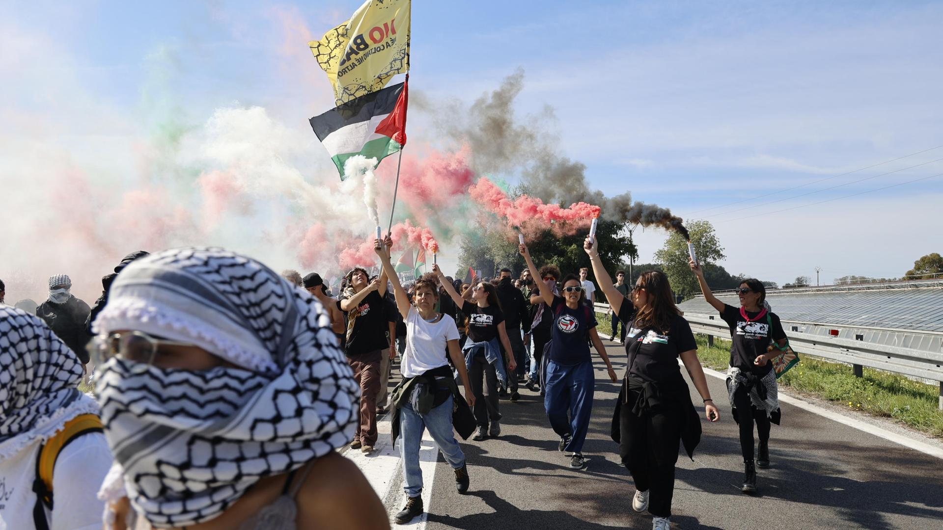 Teilnehmer eines Protestzugs sind in bunten Rauch gehüllt und ziehen über eine Autobahn 