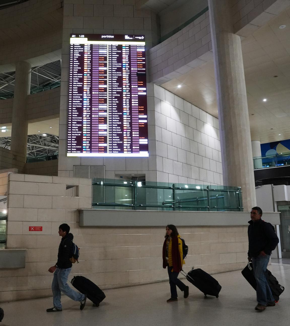 Am frühen Donnerstag, dem 11. Dezember 2025, gingen Menschen am Flughafen Lissabon an einer Anzeigetafel vorbei, auf der abfliegende Flüge, viele davon annulliert, angezeigt wurden.