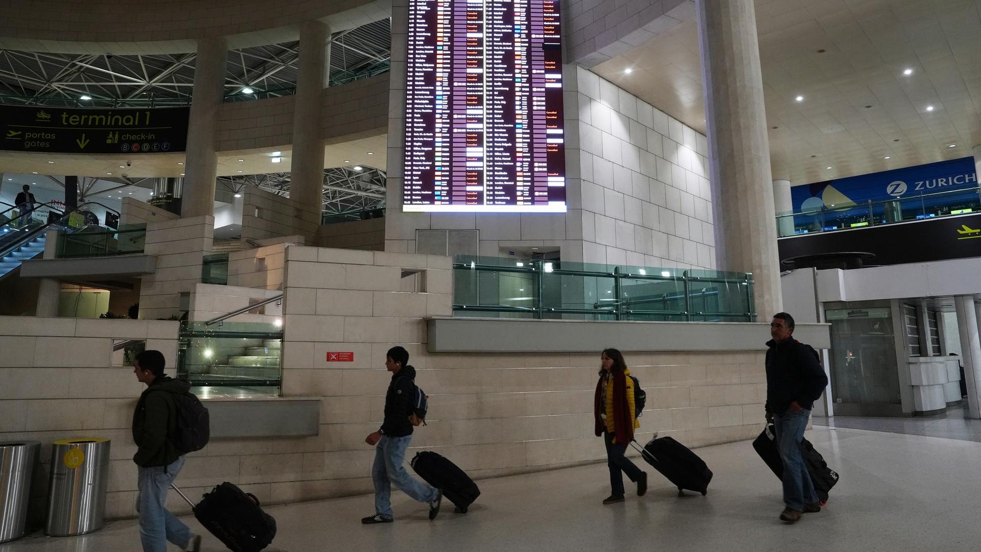 Am frühen Donnerstag, dem 11. Dezember 2025, gingen Menschen am Flughafen Lissabon an einer Anzeigetafel vorbei, auf der abfliegende Flüge, viele davon annulliert, angezeigt wurden.