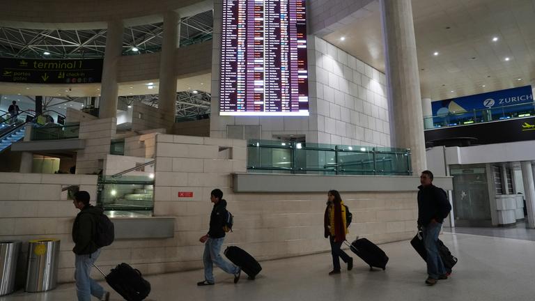 Am frühen Donnerstag, dem 11. Dezember 2025, gingen Menschen am Flughafen Lissabon an einer Anzeigetafel vorbei, auf der abfliegende Flüge, viele davon annulliert, angezeigt wurden.