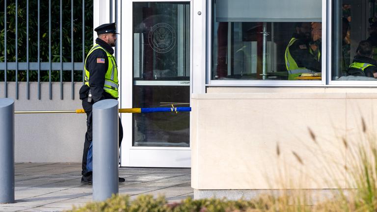 Schweiz, Genf: Ein US-Wachmann geht mit der ukrainischen Flagge vor der Ständigen Vertretung der USA in Genf, Schweiz.