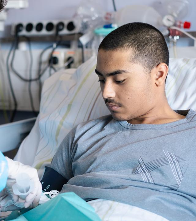 Patient Mohammed liegt in einem Krankenbett und wird von einer Ärztin behandelt. 