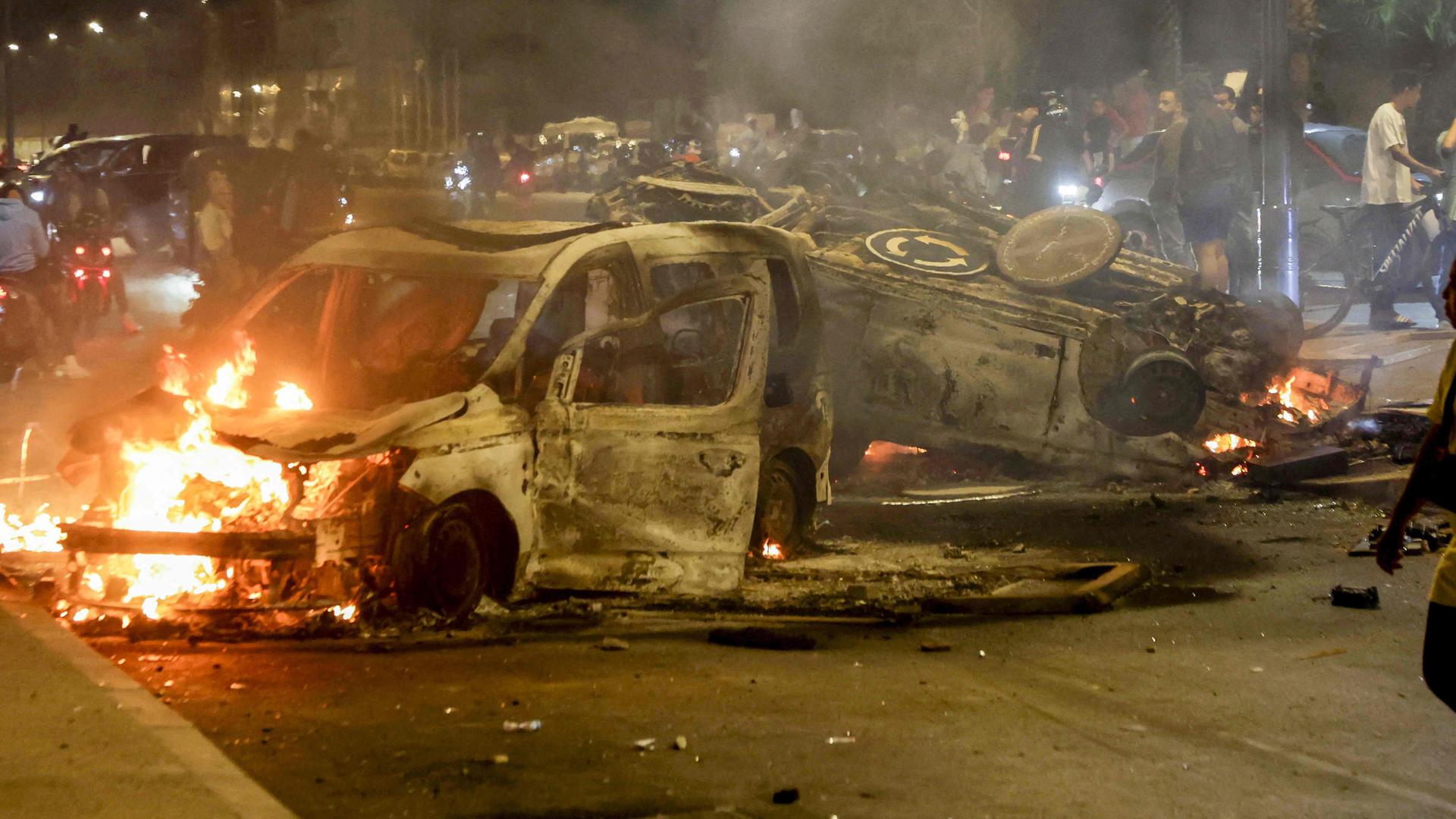 Frauen gehen an ausgebrannten Polizeifahrzeugen vorbei, die bei einer von Jugendlichen geführten Demonstration für Reformen im Gesundheits- und Bildungswesen in Salé in Brand gesetzt wurden. Aufgenommen am 01.10.2025.