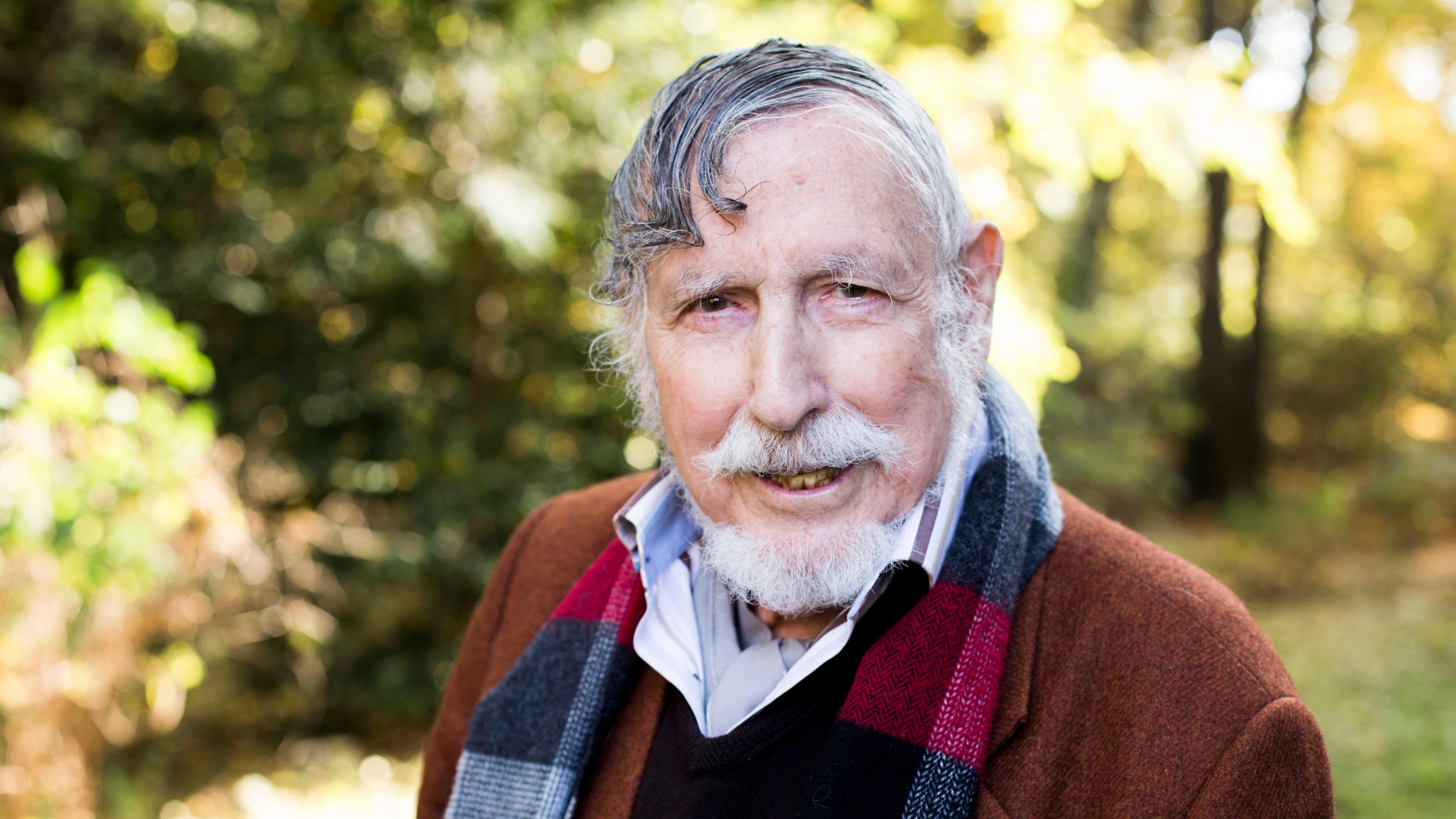 Georg Stefan Troller. Er trägt einen weißen Bart. Im Hintergrund sind Bäume und Büsche zu erahnen.